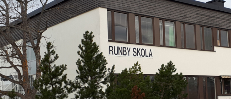 Skolbyggnadsfasad i vit puts och brunt trä. Skylt som säger Runby skola.