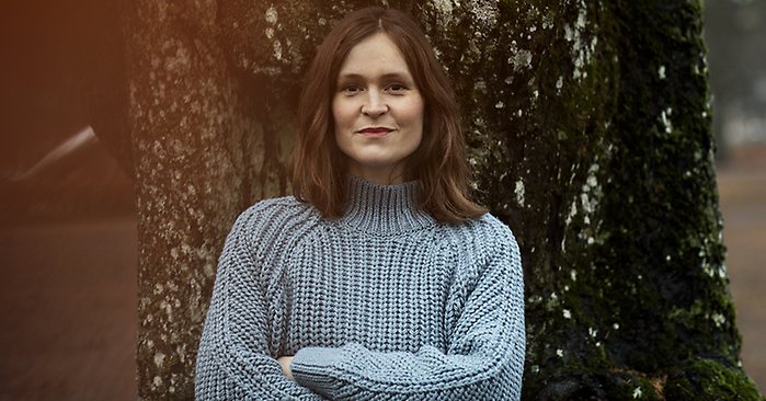 Porträttfoto på författaren Elin Cullhed. Hon står med armarna i kors i en stickad tröja framför en stor trädstam.