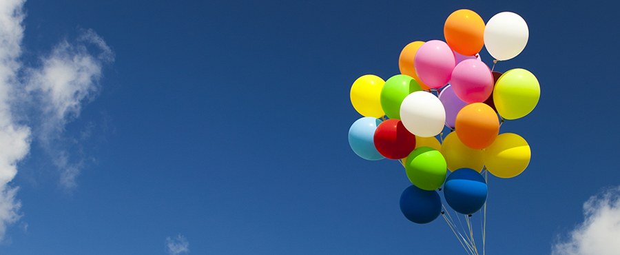 Flera ballonger som en bukett hålls mot en blå himmel. 