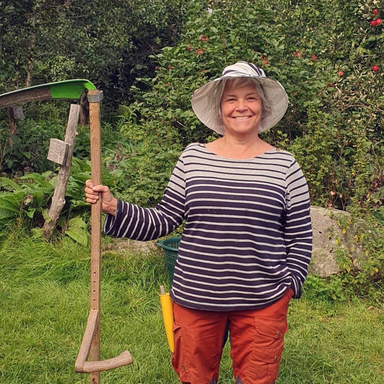 Pia Cederberg från Jordnära bildning står i en trädgård med en lie i handen