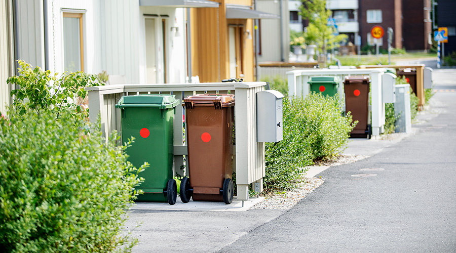 Bilden innehåller två olika sopkärl som är grön och brun sopkärl längs en gata med radhus  