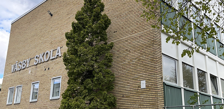 Bild på Väsby skolas fasad, en gul tegelvägg med texten Väsby skola.