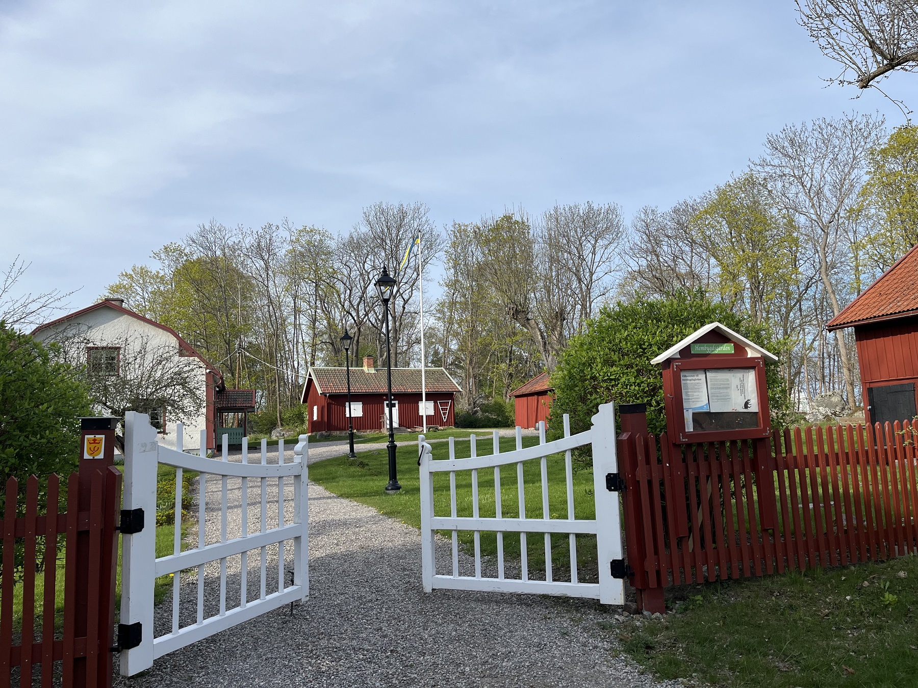 Vy över hembygsgården, grusgång leder in till föreningens rödmålade byggnader.