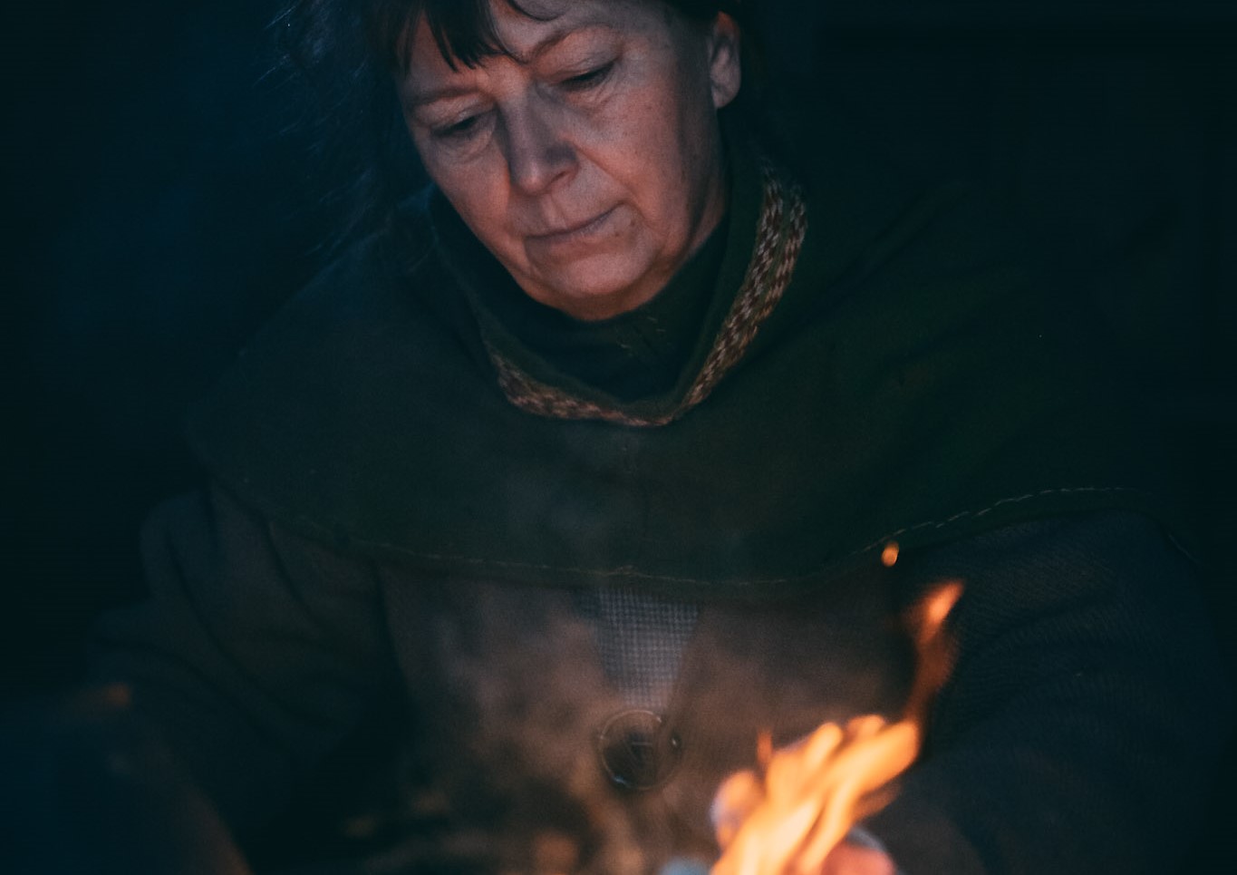 En kvinna som tittar ner mot marken. Framför henne finns en liten eld.