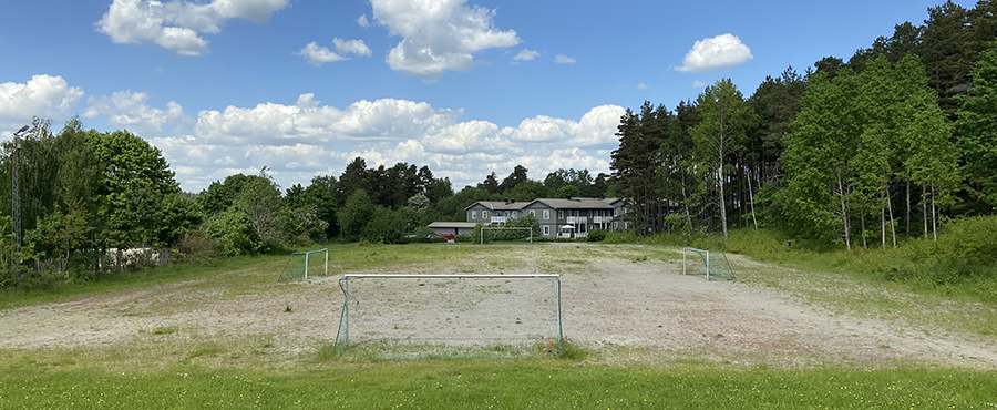 En grusplan med två fotbollsmål. I bakgrunden syns ett par gråa hus.