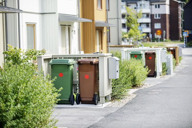 Gröna och bruna sopkärl utanför hus i ett bostadsområde.