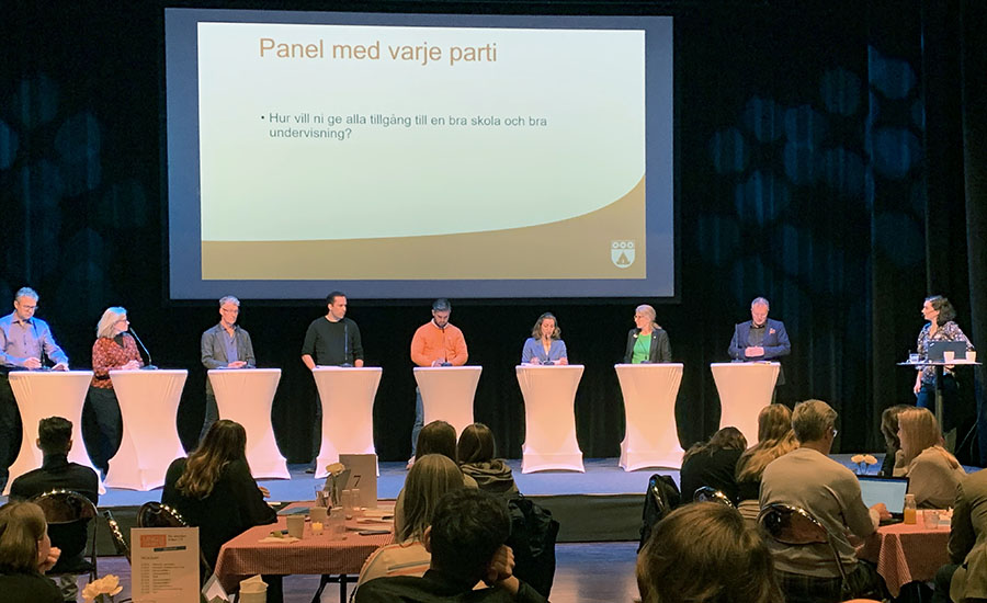 Ett 10-tal personer på en scen bakom vita podium.