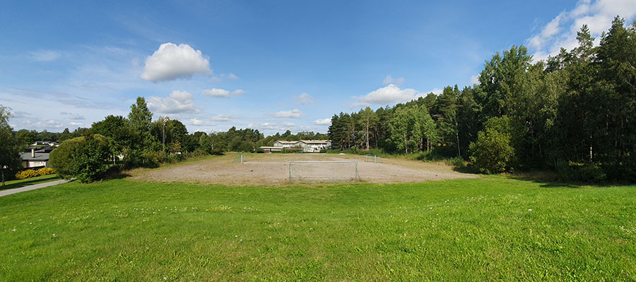 En vidvinkelbild över en fotbollsplan med grönt gräs och skog runtom.