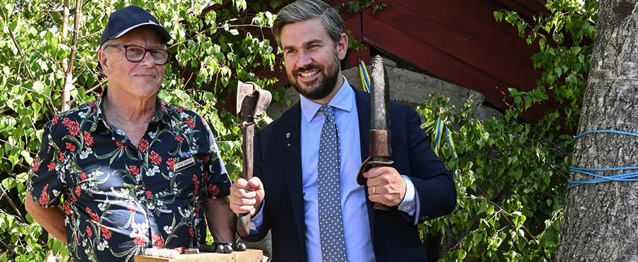 Hans och Oskar syns på bilden. Oskar håller två verktyg från när graven anlades. Hans håller i en bricka av trä. I bakgrunden syns gravhögen.