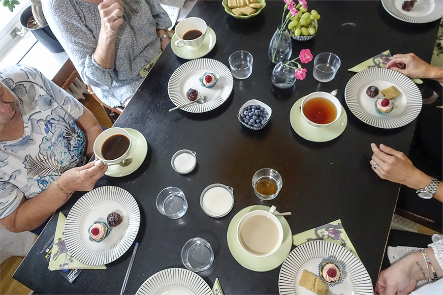 Fikabord med kaffe och kakor och människor runt bordet.