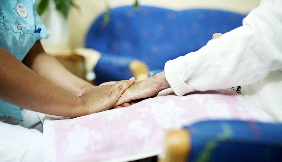 En sköterska håller en äldre persons händer.