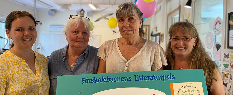 Fyra personer tittar in i kameran och håller upp ett stört diplom.