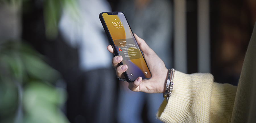 En person håller upp en mobiltelefon med en varningsnotis på skärmen.