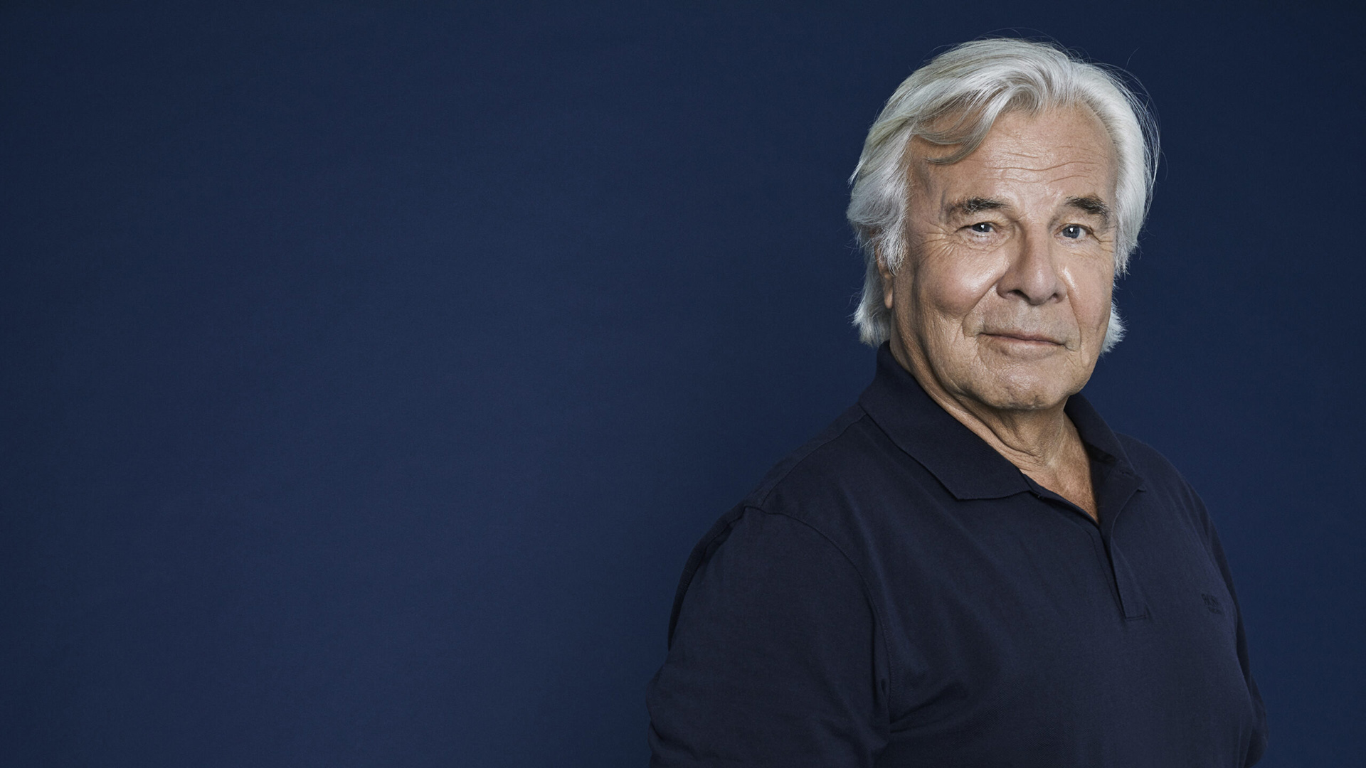 Jan Guillou tittar mot kameran. Han har ljust hår och en skjorta.