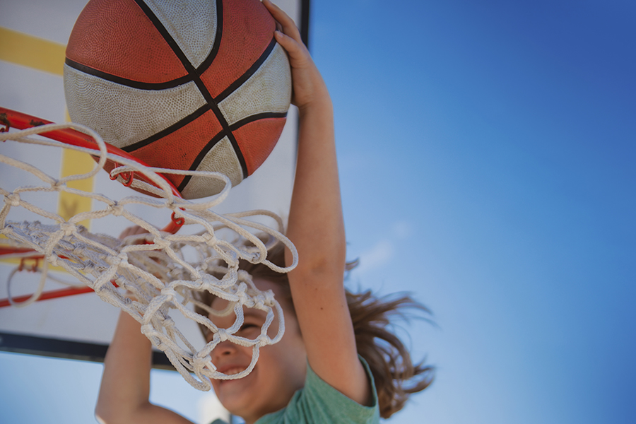 Ett barn hoppar upp mot en basketkorg och placerar bollen i korgen.