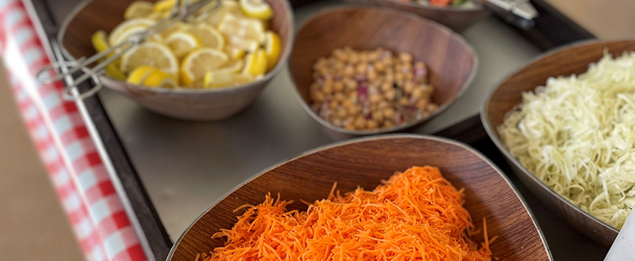Riva morötter i en skål och i bakgrunden syns flera skålar med grönsaker.