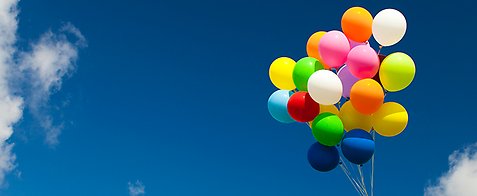 Flera ballonger som en bukett hålls mot en blå himmel.