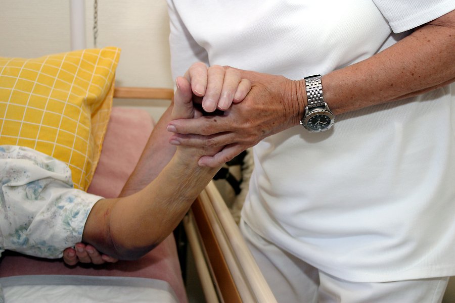 En vårdanställd håller en äldre patient i handen.