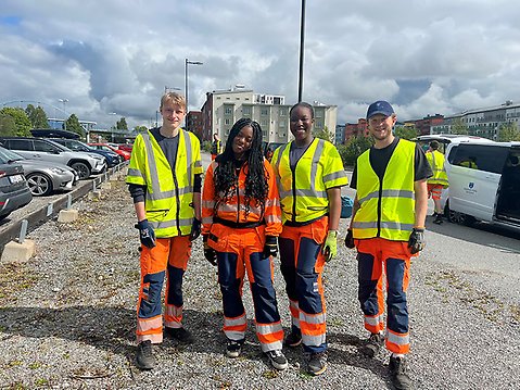 De fyra sommarjobbarna står på en rad bredvid varandra. De har på sig orangea arbetskläder och gula varselvästar. Alla ler och tittar in i kameran.