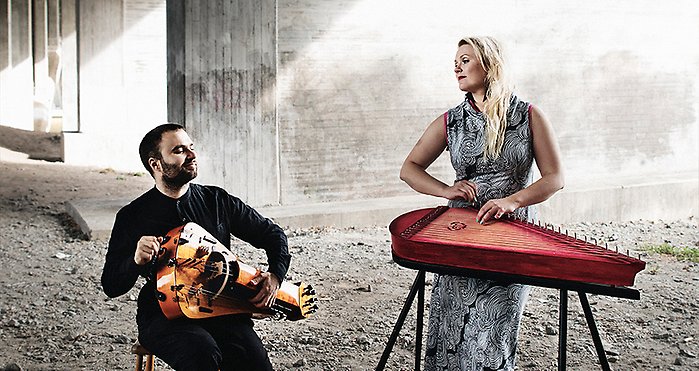En  man som sitter och spelar vevlira och en kvinna som står bakom en kantele.