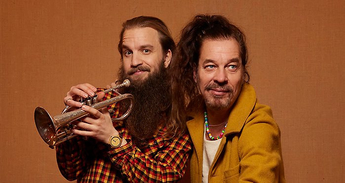 Två glada män varav en håller en trumpet