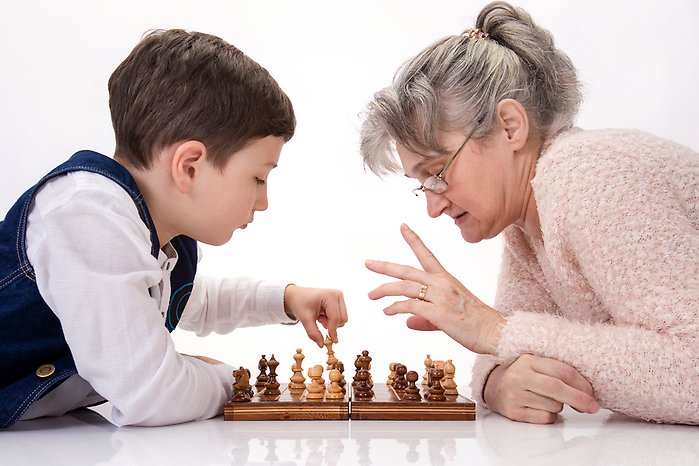 En ung pojke spelar schack med en äldre dam.