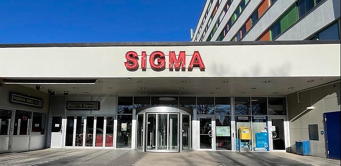 Sigma Centrums entré med den röda skylten där det står "Sigma centrum" och en klarblå himmel bakom