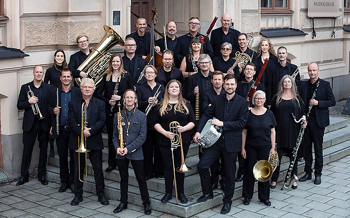 En stor blåsorkester stående på en entrétrappa med sina instrument i händerna