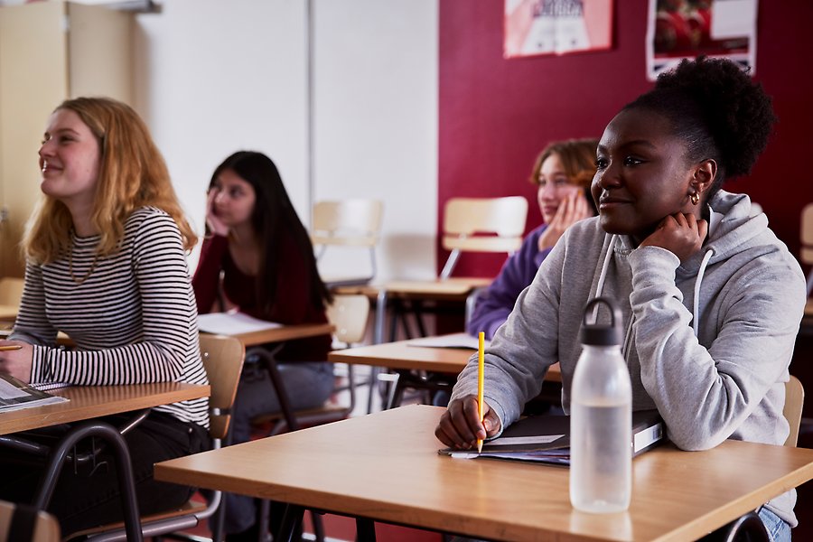 Några elever sitter i ett klassrum och lyssnar på läraren.