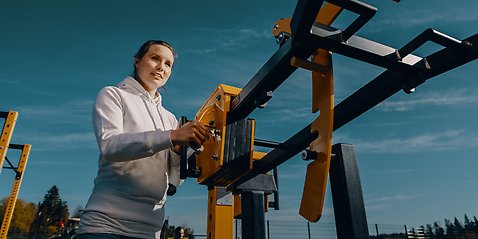 Kvinna som håller i ett gult träningsredskap på ett utegym