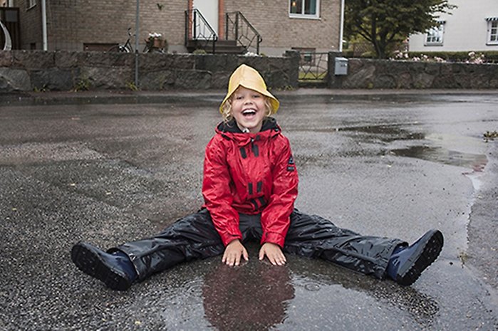 Det regnar och ett barn sitter i en vattenpöl
