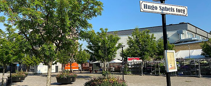 Bild på Hugo Sabels torg där det finns blommor i urnor, träd med gröna löv, blomsterförsäljning och vagnar med matförsäljning. 