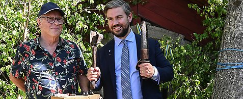 Hans och Oskar syns på bilden. Oskar håller två verktyg från när graven anlades. Hans håller i en bricka av trä. I bakgrunden syns gravhögen. 