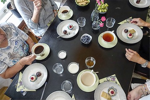 Fikabord med kaffe och kakor och människor runt bordet.