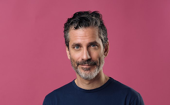 Bild på författaren Jens Lapidus, i blå t-shirt, mot lila bakgrund.