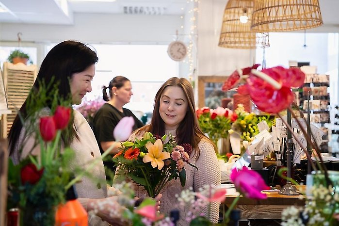 Två personer som jobbar i en blomsterbutik sätter ihop en blombukett tillsammans.