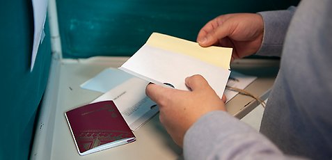 Hand som håller i ett valkuvert i ett valbås.