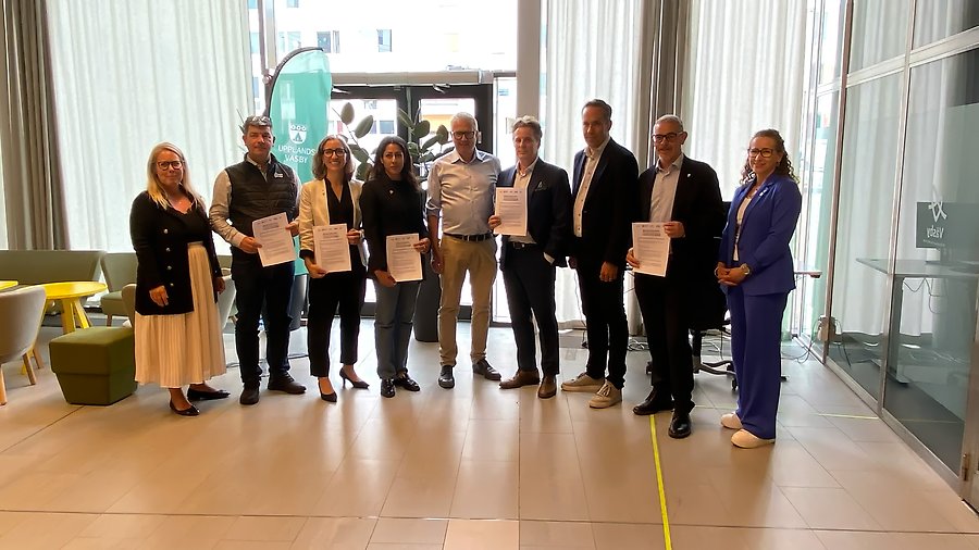 En grupp personer, män och kvinnor står uppradade bredvid varandra med dokument i händerna.
