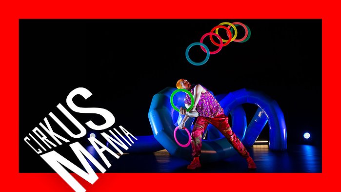 En man jonglerar med ringar framför en hög med slingrande plaströr. Allt i neonfärger.