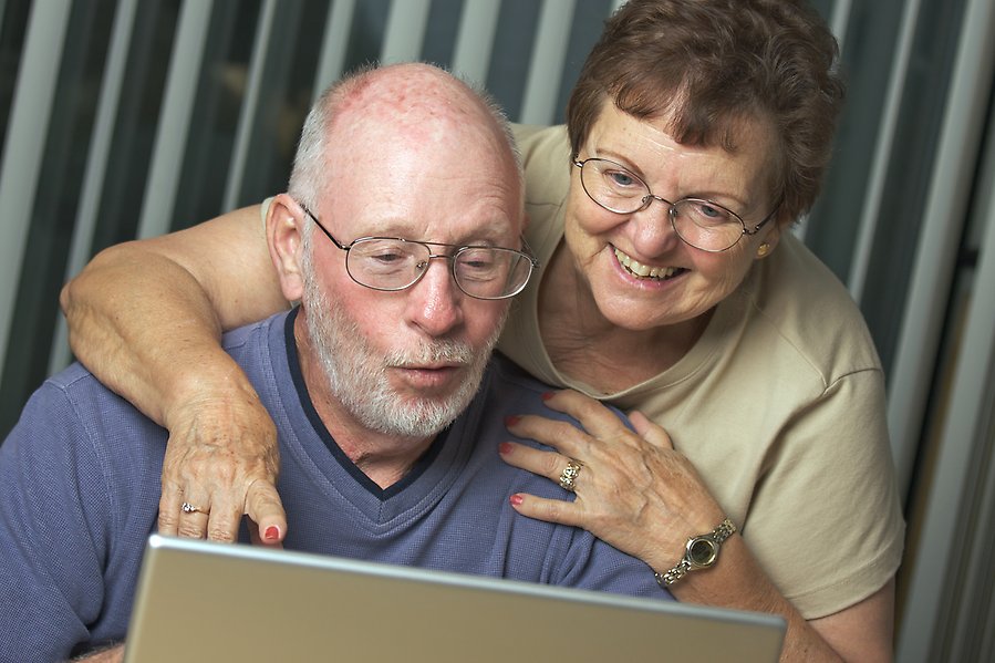 En man sitter framför en dator och en kvinna lutar sig över honom bakifrån för att kika på skärmen