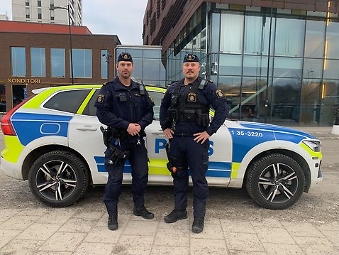 Två poliser står framför en polisbil utanför byggnaden Messingen. 