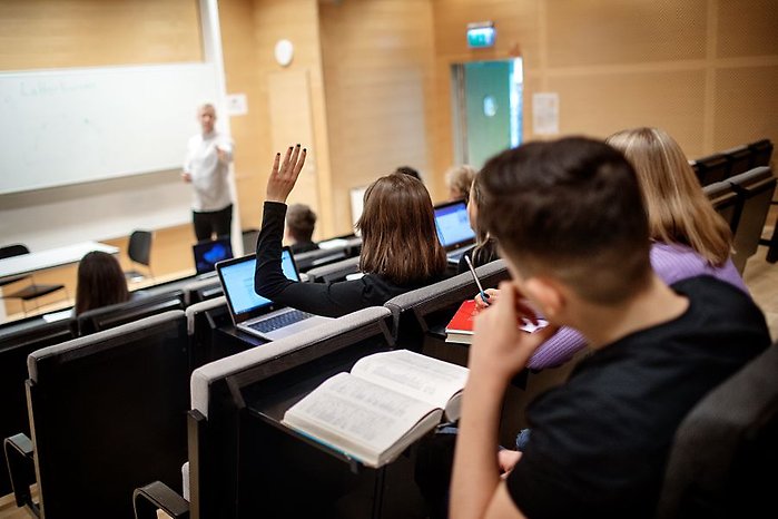 Elever på lektion i aula med lärare som undervisar.