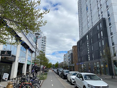 Bild från en gata med parkerade bilar och byggnader på båda sidor av vägen.