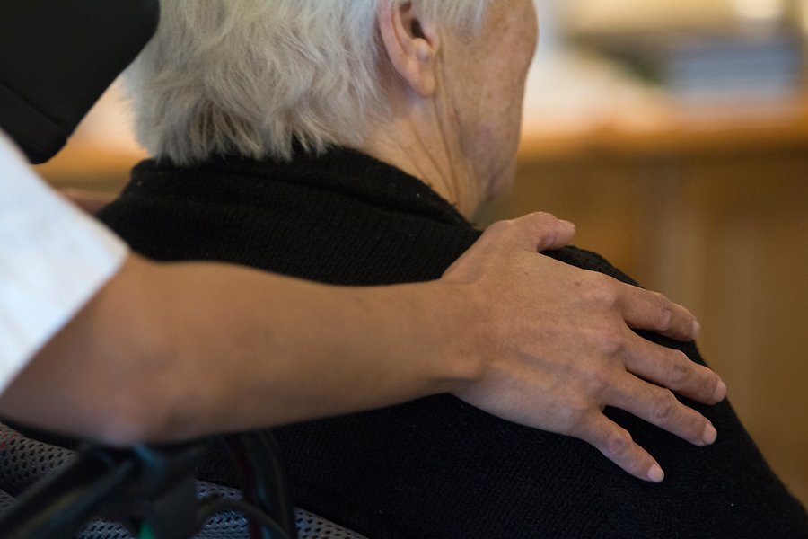 En vårdanställd håller sin hand på en äldre kvinnas axel.