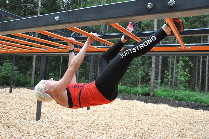 Kvinna klättrar upp och ner på ett redskap på ett utegym.